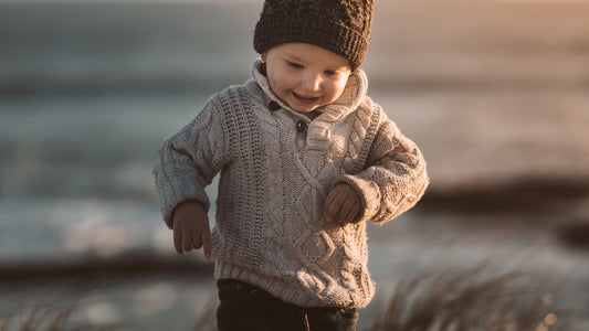Toddler in a toque and sweater running on a beach in the fall.