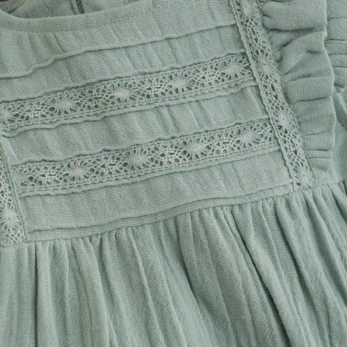 Close up product image of a light green muslin baby dress