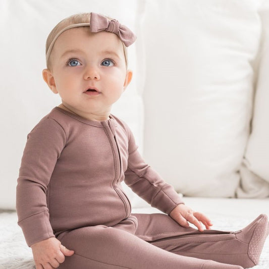 Baby seated in a mauve zipper sleeper