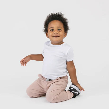 Smiling toddler sitting on knees wearing a white top and light pink sweatpants