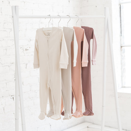 Four baby sleepers hanging on a clothing rail in earthy pink shades and beige neutrals