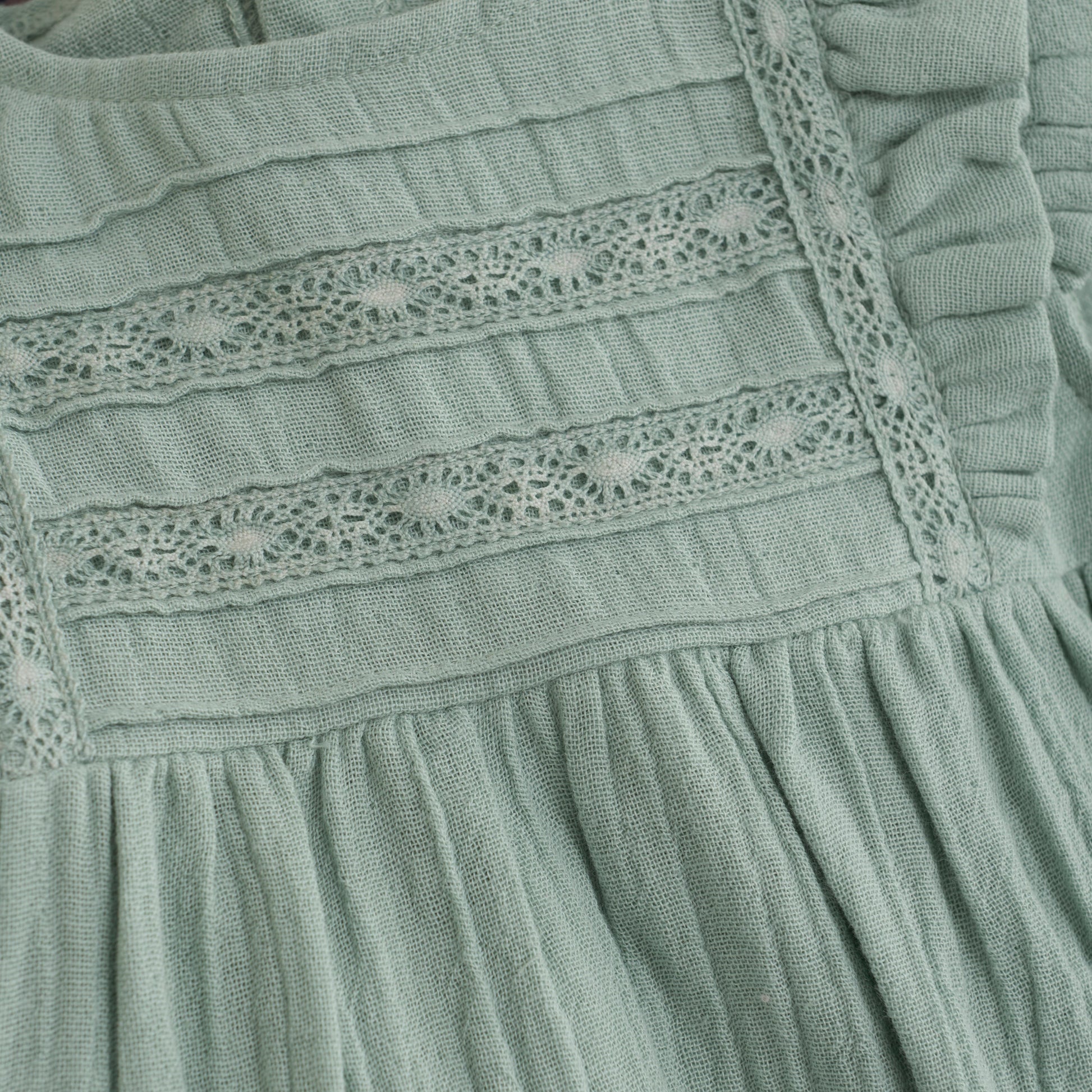 Close up product image of a light green muslin baby dress