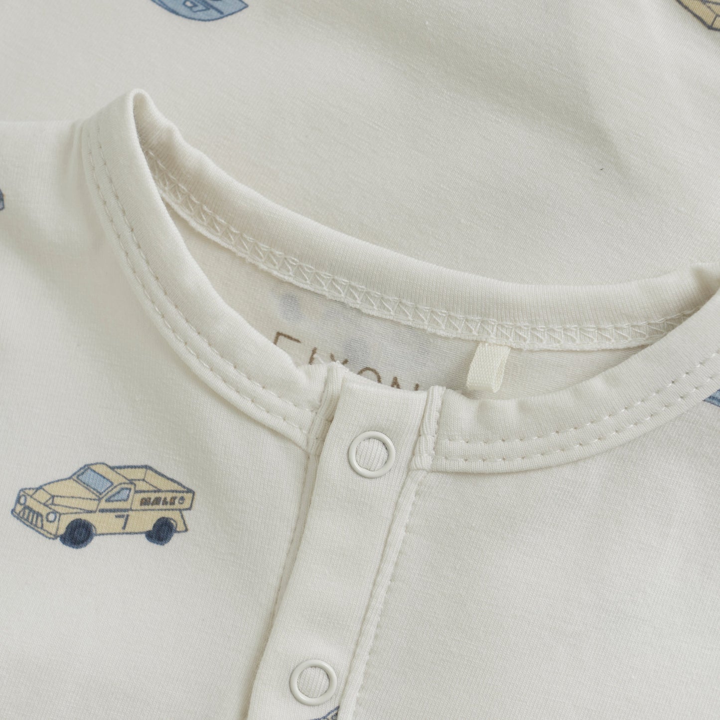 Close up product image of ivory baby playsuit with car print