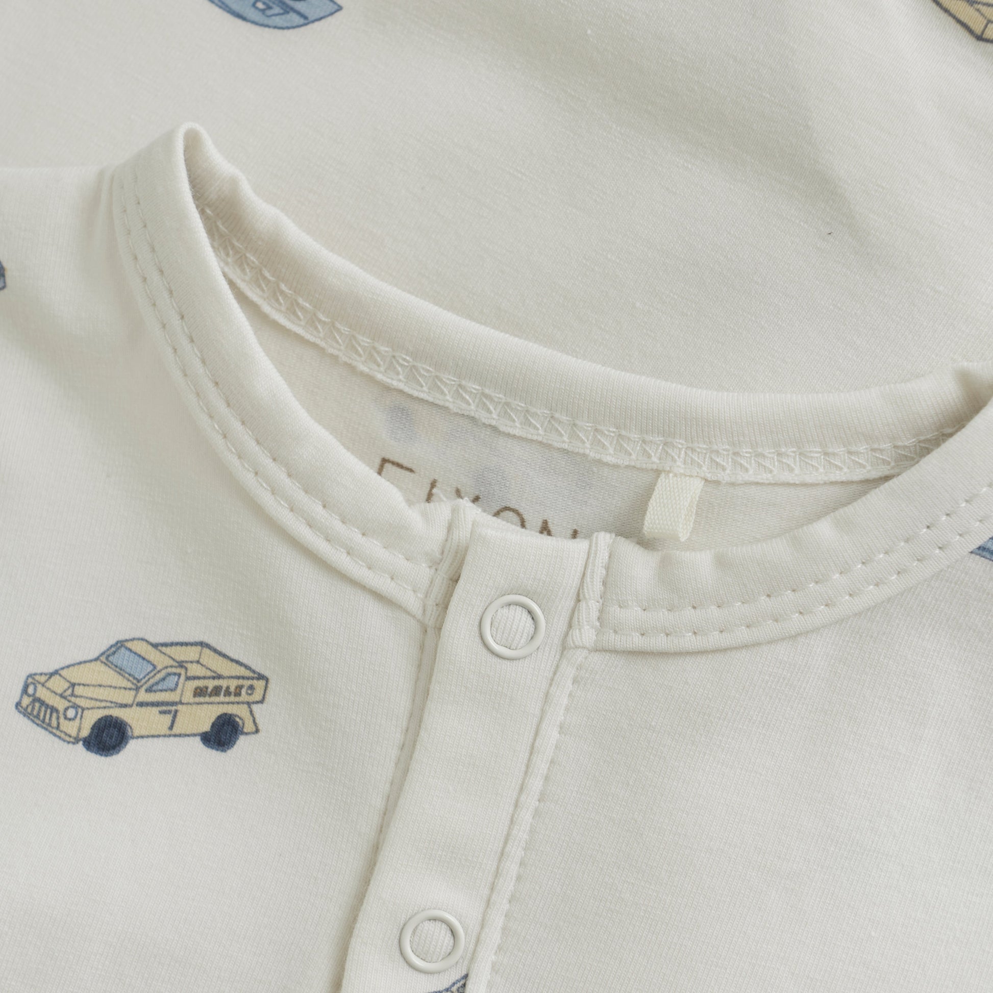 Close up product image of ivory baby playsuit with car print