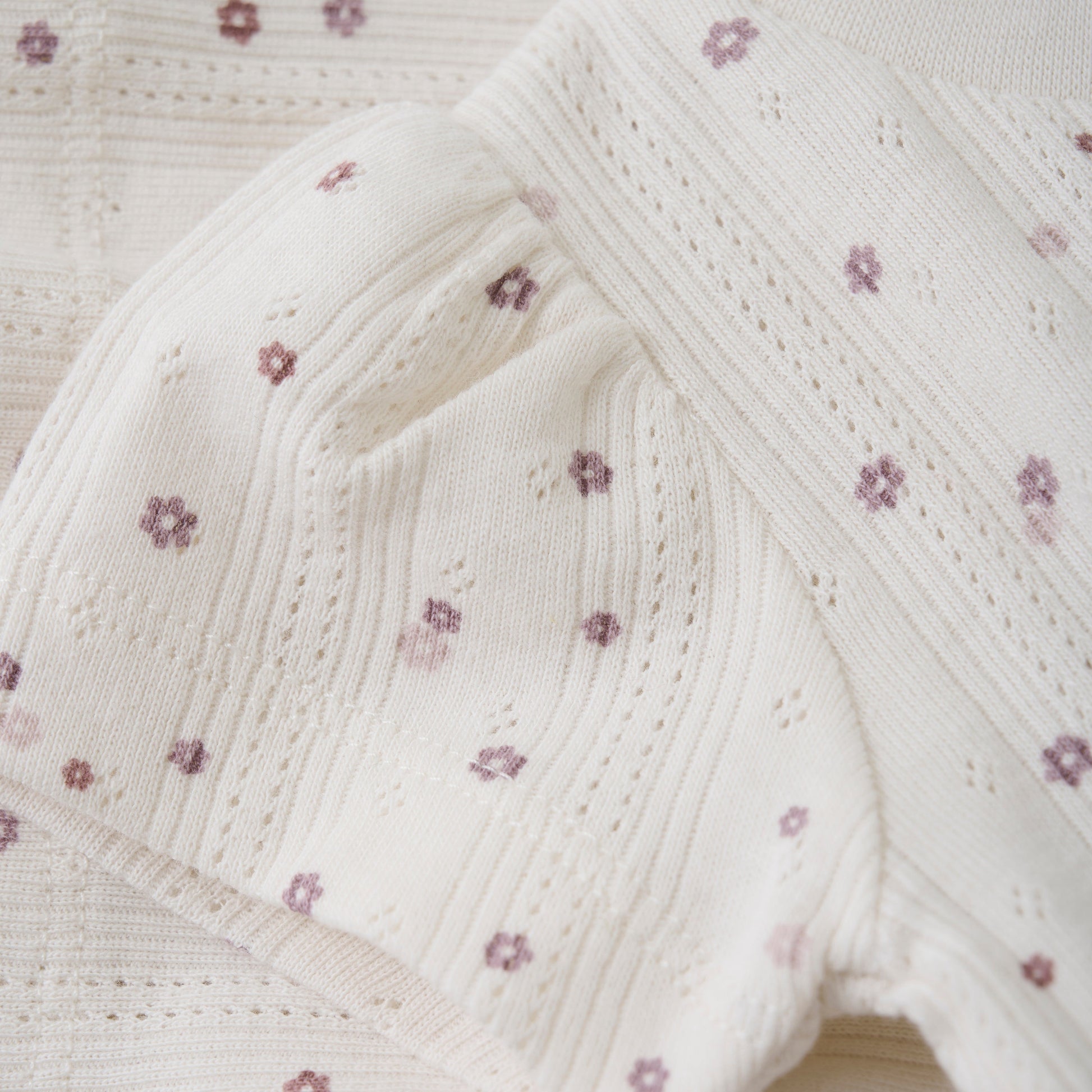 Close up product image of an ivory pointelle baby tee with a purple daisy print