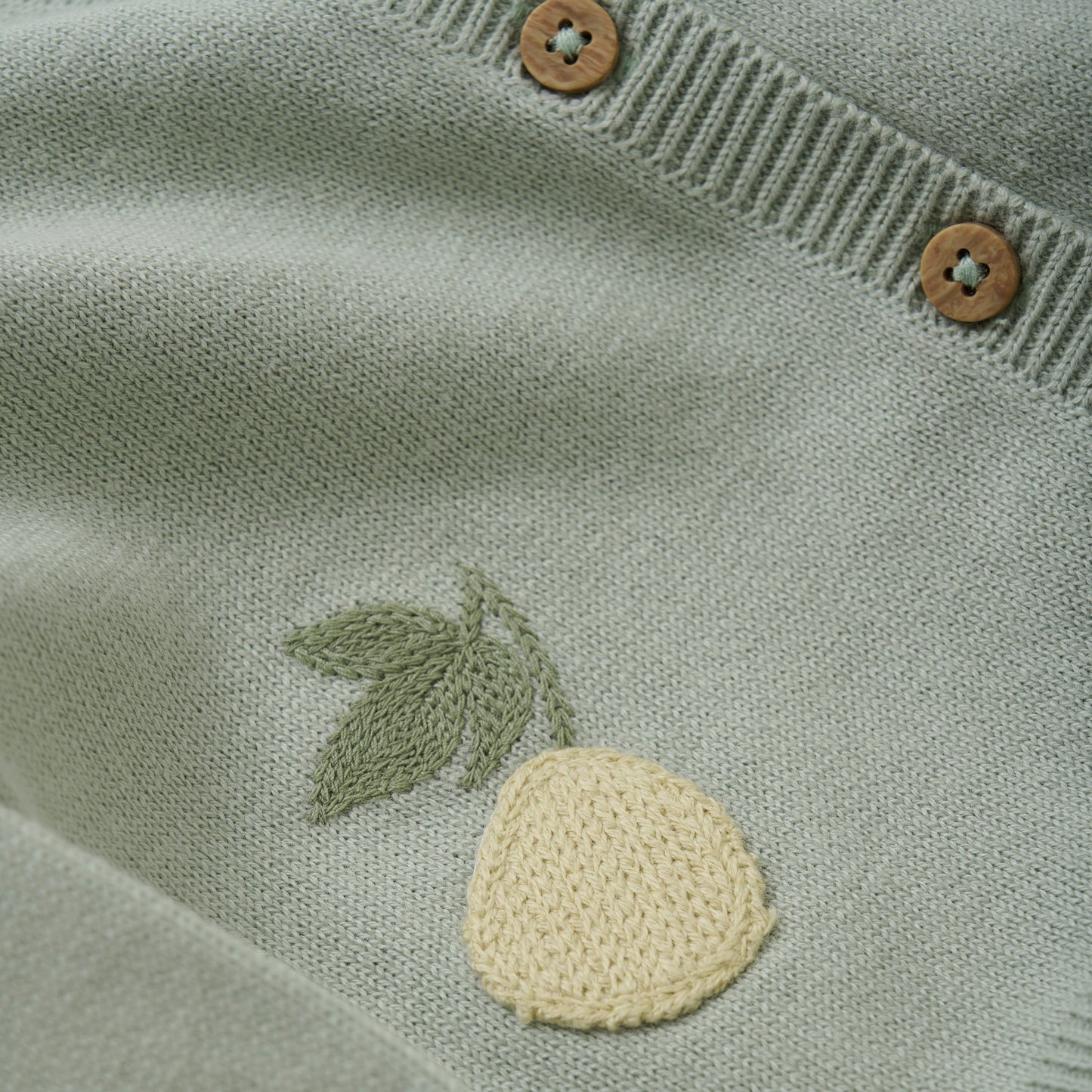 Close up product image of a soft green knit baby cardigan with small pineapple embroidery