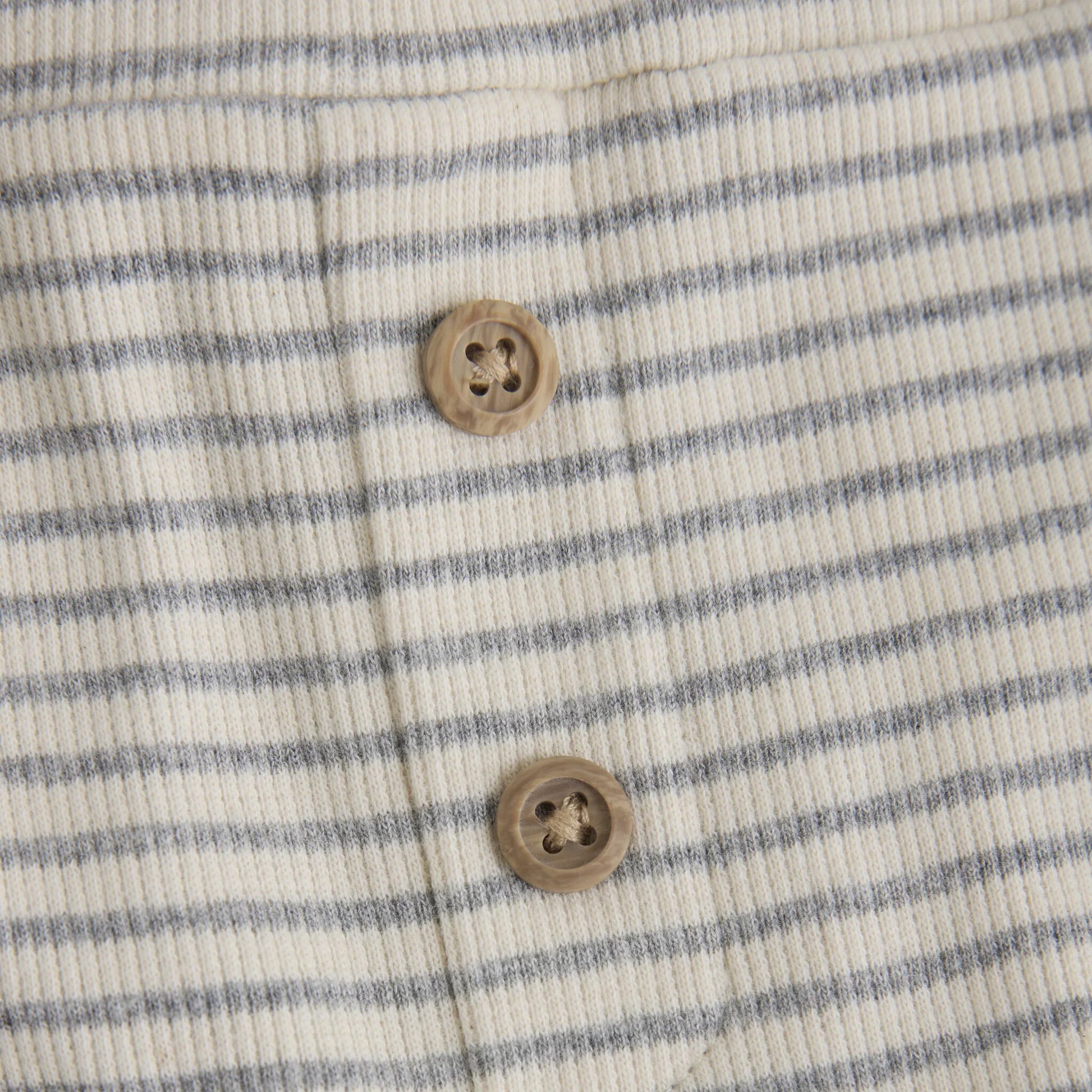 Close up product image of baby leggings with two small wooden buttons in light grey stripes on ivory