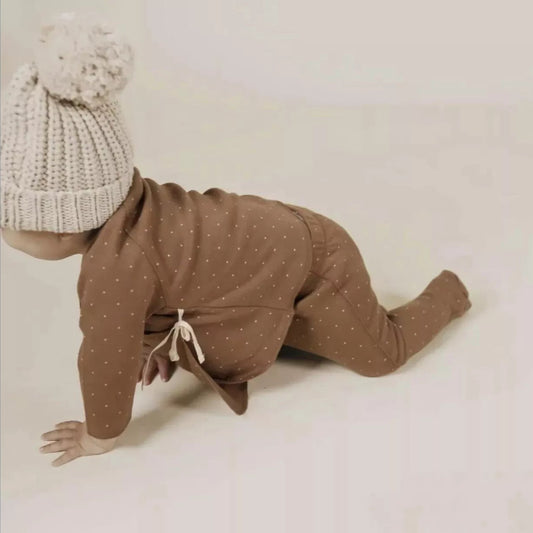 Baby wearing a wrap top and pant set with a knit toque crawling away from the camera