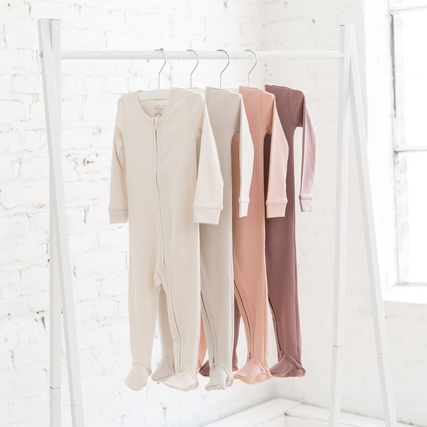 Four baby sleepers hanging on a clothing rail in earthy pink shades and beige neutrals