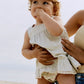 Lifestyle product image of baby in a dress playing on the beach